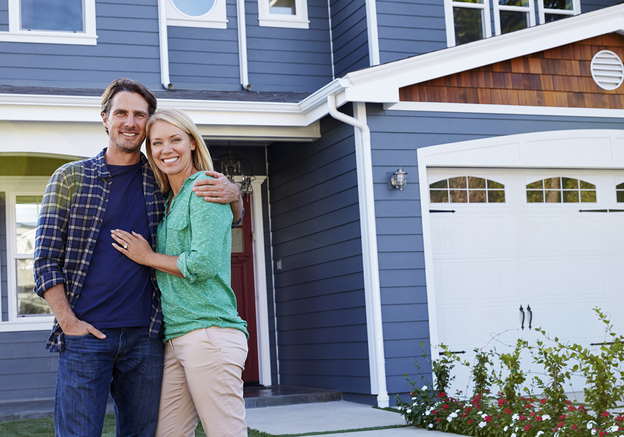 Smiling Couple Standing Outside Home with Modern Garage Door